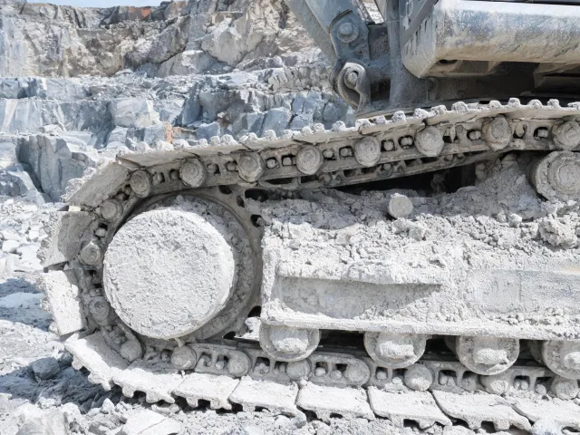 Hard-rock quarry excavator undercarriage in dust